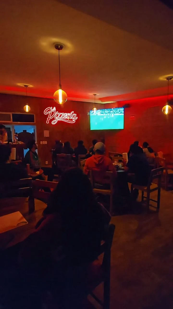 Ambiente real de La Pizzería con iluminación roja y mesas